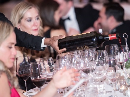 Server reaching between two women to pour red wine